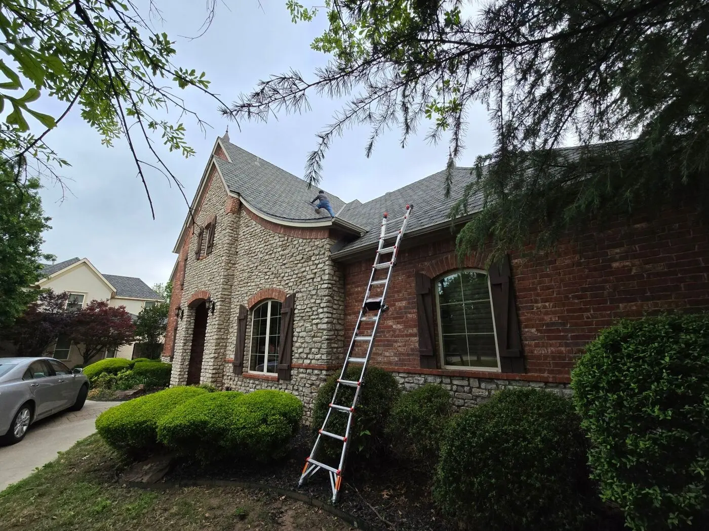 Roofing crew member working on the roof of a stone and brick tudor-style home