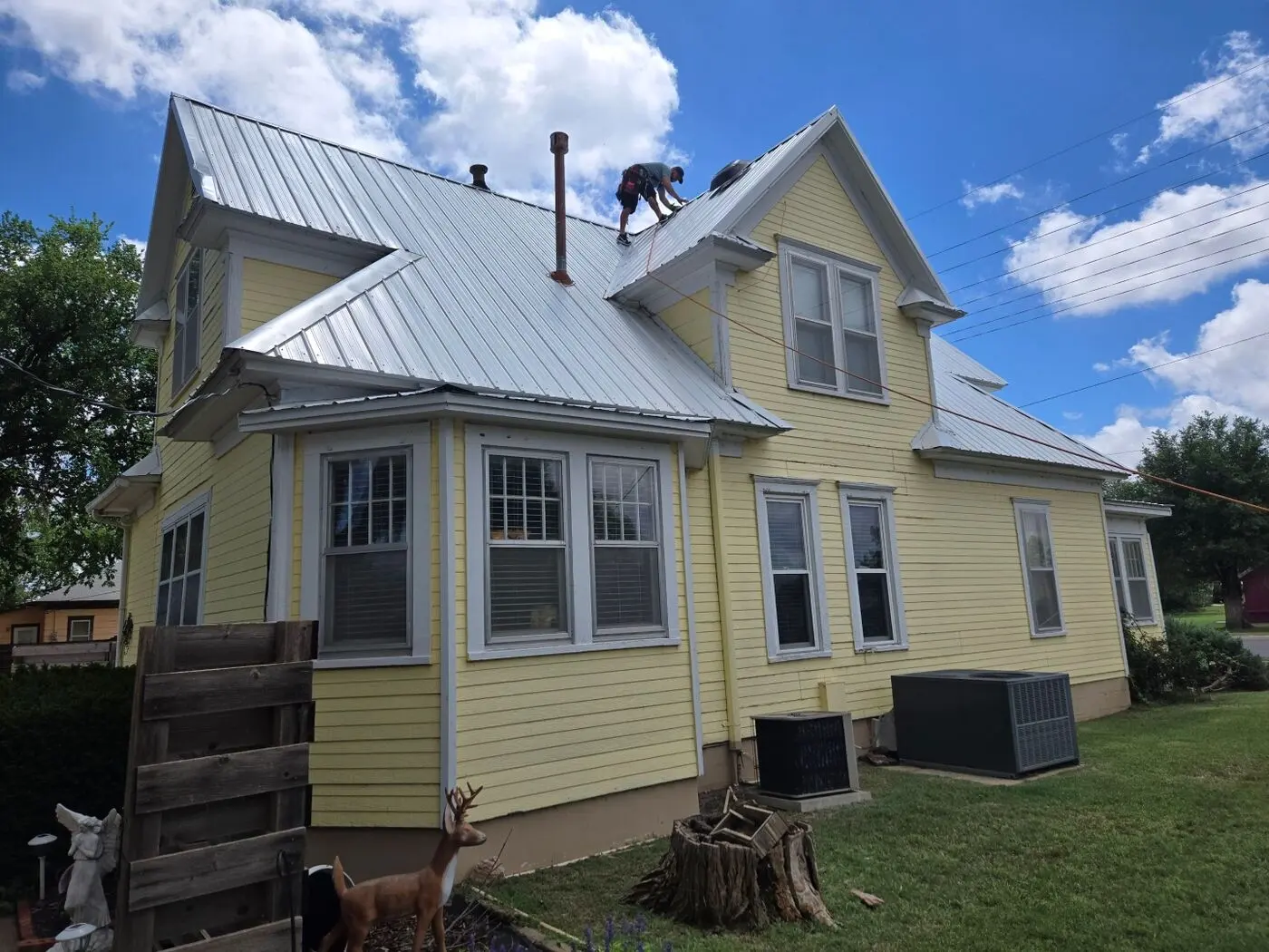 Crew member installing a metal roof on a yellow historic home